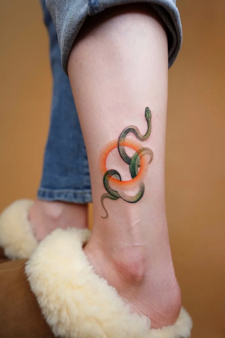 A colorful snake tattoo rendered in a watercolor style with an orange halo surrounding the serpent's body.
