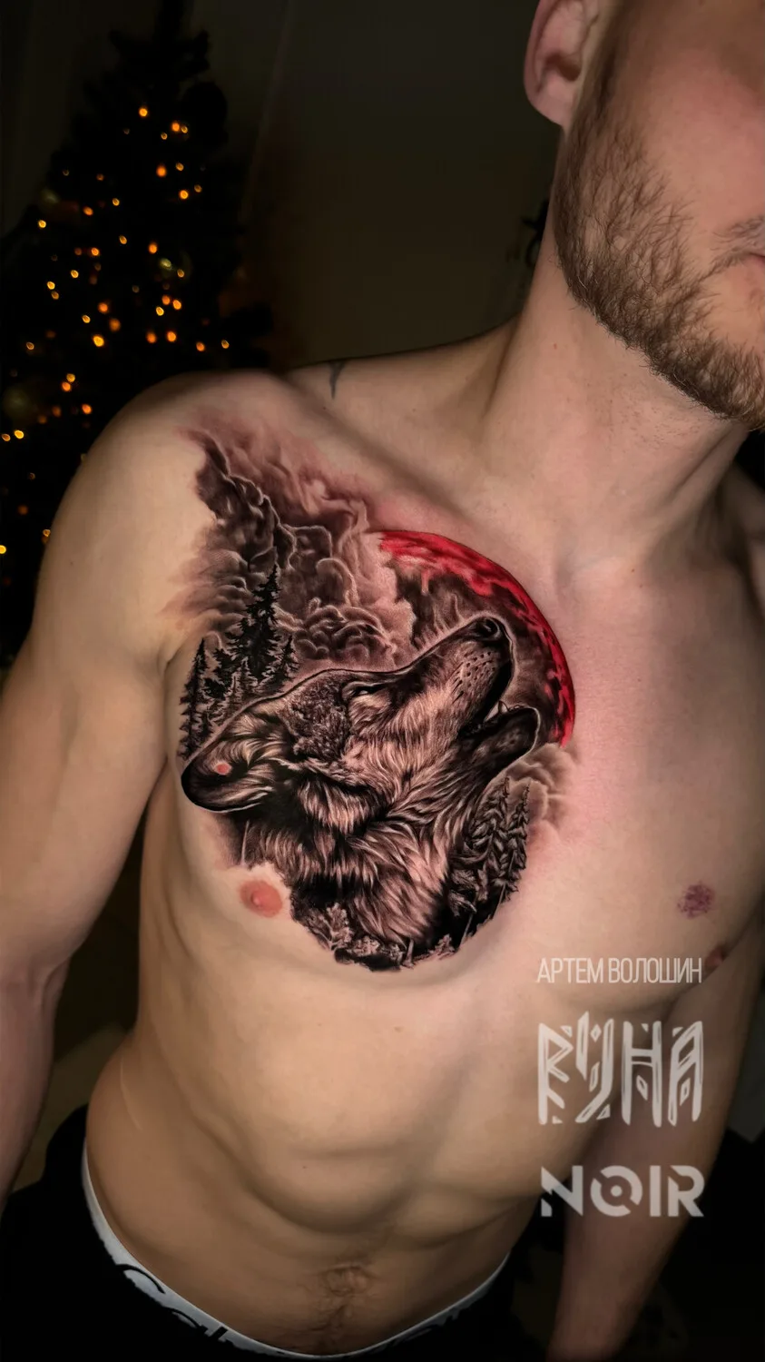 A detailed black and grey tattoo of a wolf howling at a red moon, set against a backdrop of trees and clouds.