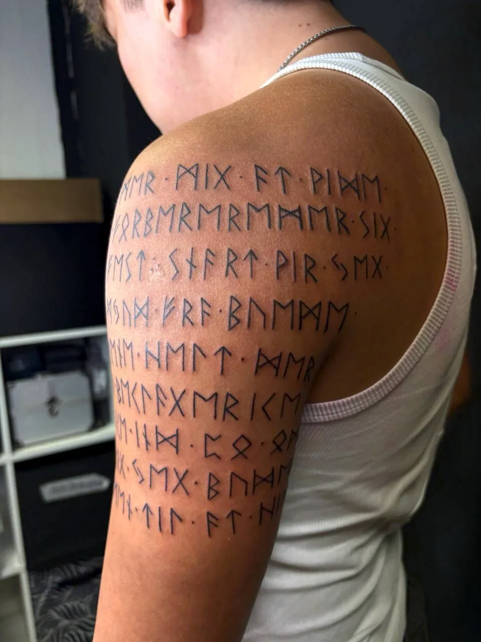 Ein Blackwork-Tattoo mit runischer Schrift, die den Oberarm bedeckt.