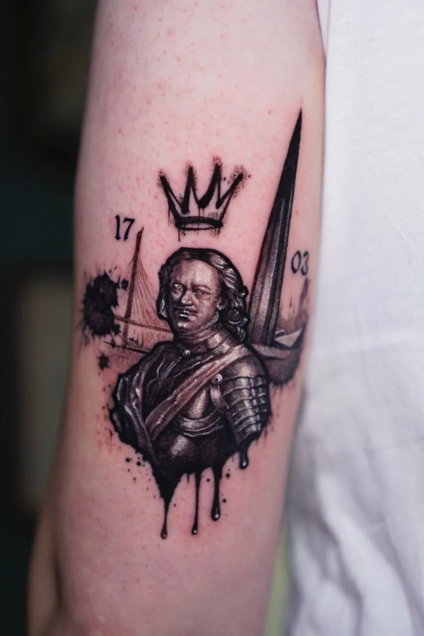 Tatuaggio realistico in bianco e nero di una figura storica corazzata in busto, incorniciata da una corona, un veliero, una lama e le cifre 1703, con accenti di inchiostro schizzato.