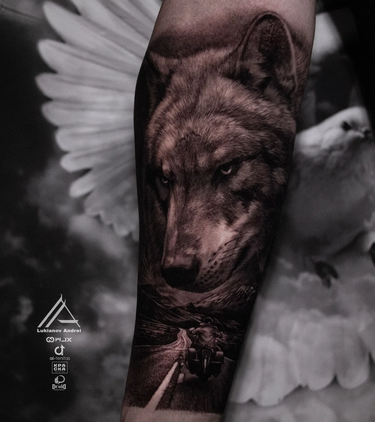 A detailed black and grey tattoo featuring a wolf's head and a biker on a road.