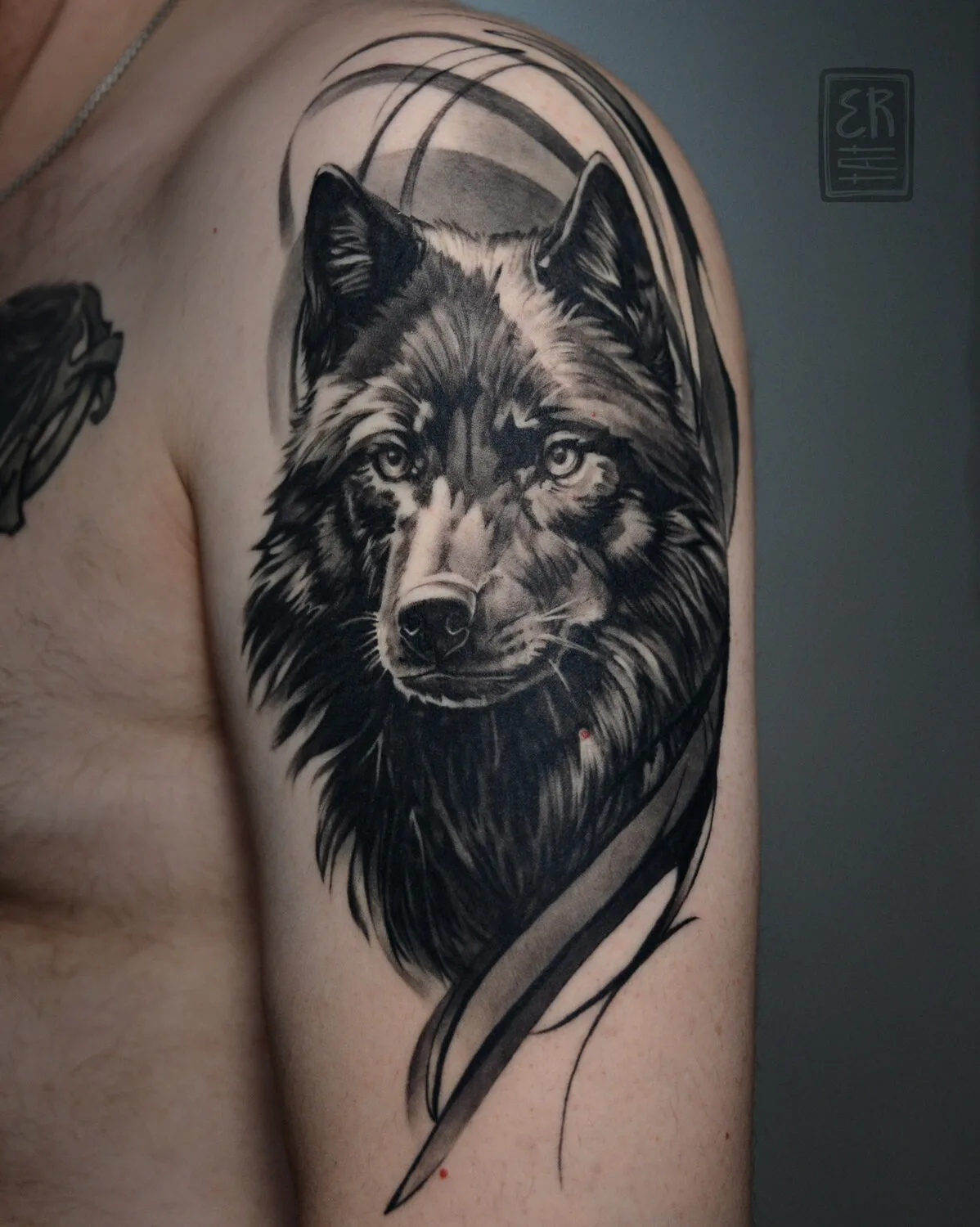 A detailed black and grey tattoo of a wolf's head with abstract elements.