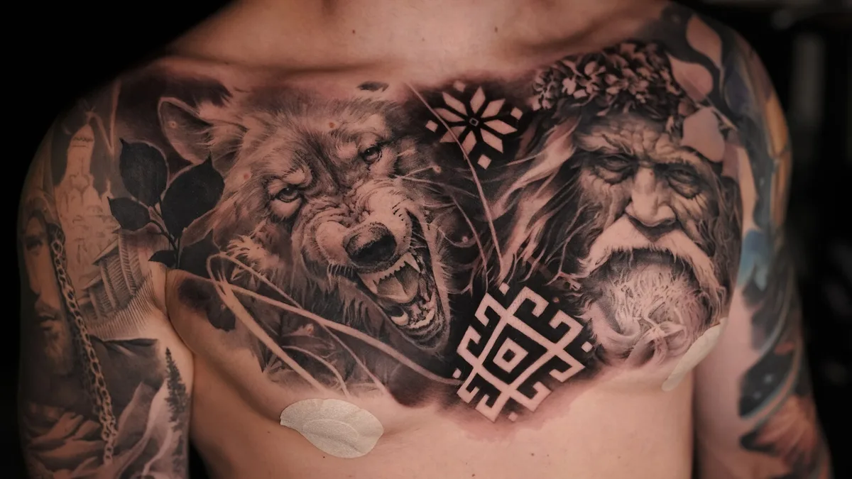 A detailed black and grey chest piece featuring a snarling wolf and a detailed portrait of an old man, with geometric elements.