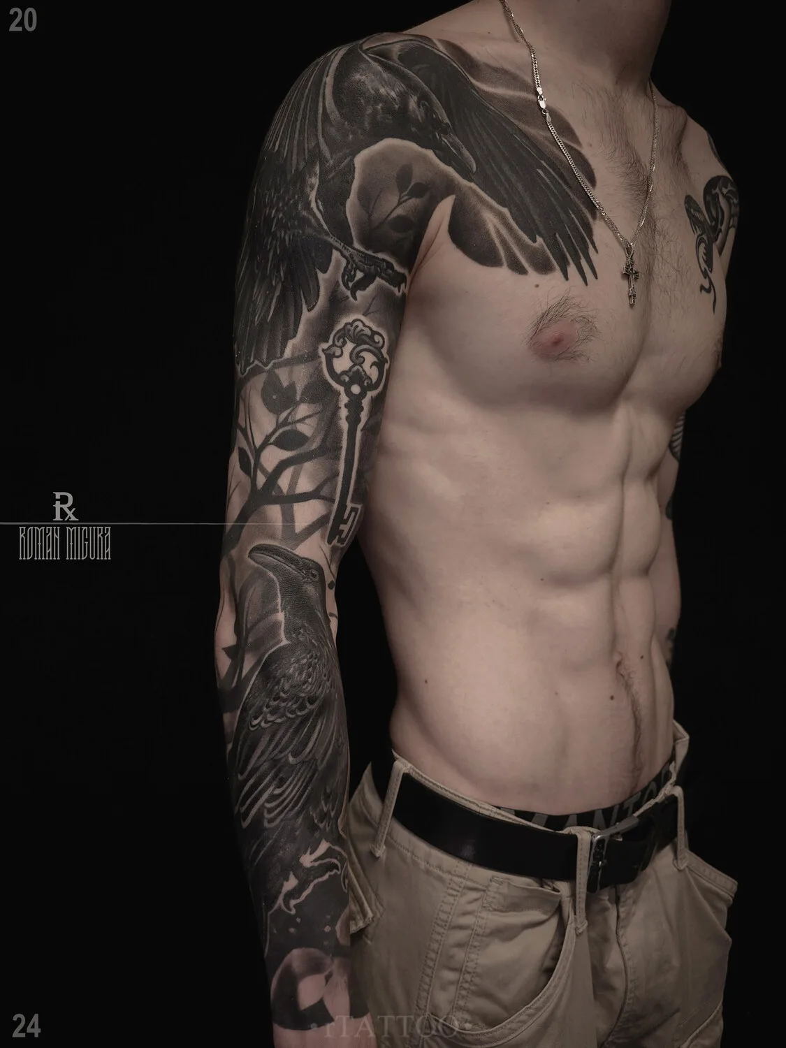 A detailed black and grey full arm tattoo featuring a raven holding a key among bare branches, covering the entire arm with fine linework and shading.