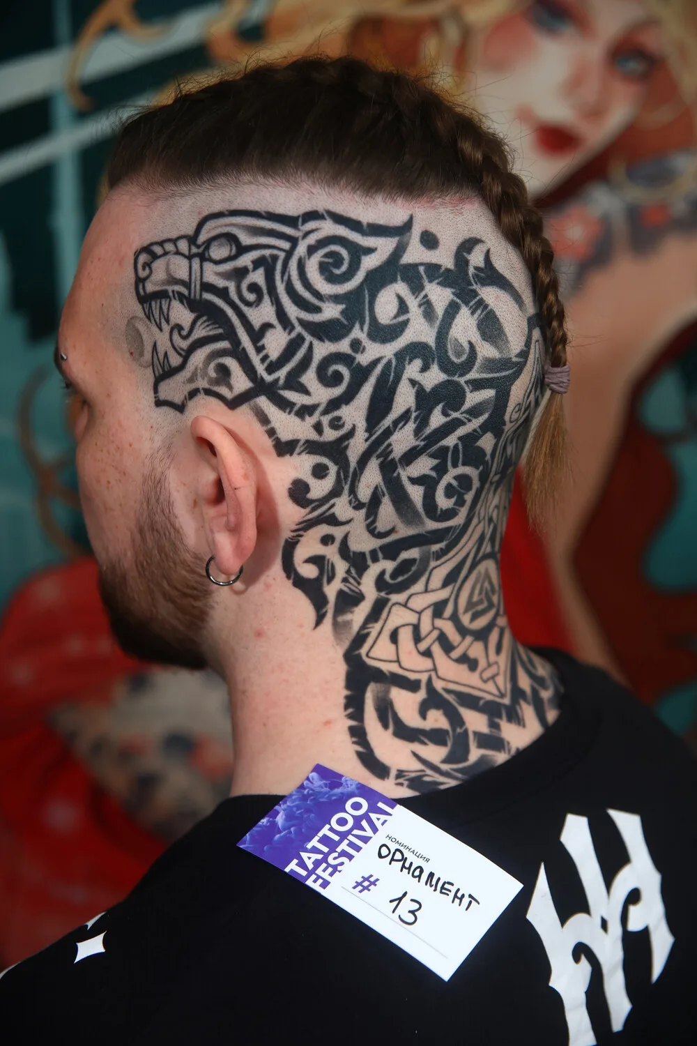 Ein Blackwork-Tribal-Tattoo auf Kopf und Hals mit einem knurrenden Wolfskopf, Flechtwerk und einem Valknut-Symbol.