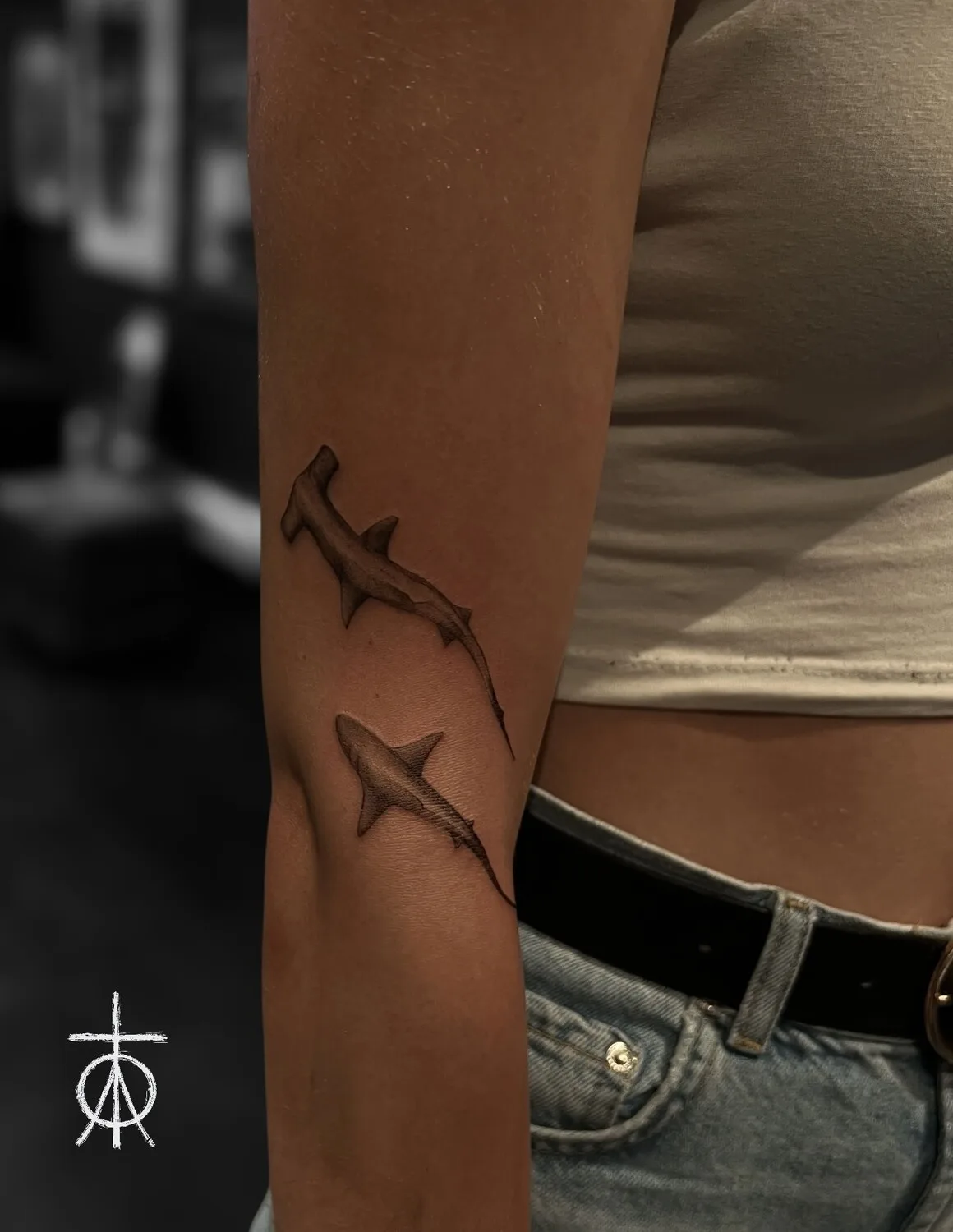 Two realistic fine-line black and grey hammerhead shark tattoos placed side by side on the forearm, with detailed shading and smooth linework.