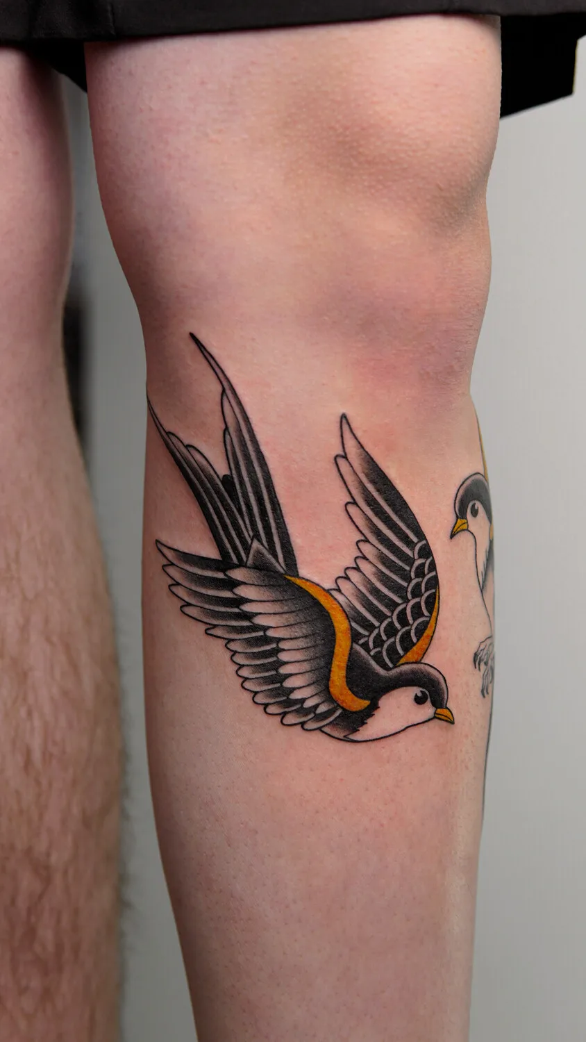 Ein Traditional-Tattoo einer Schwalbe in Schwarz, Gelb und Weiß auf dem Oberschenkel.