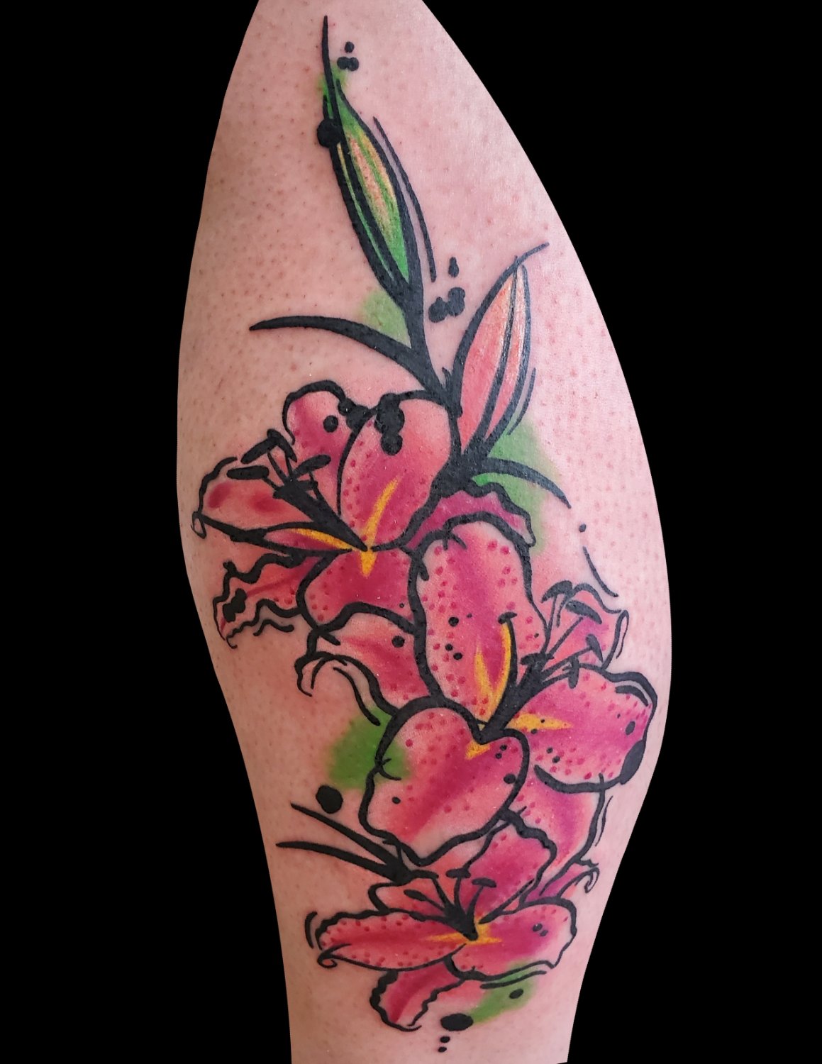 A tattoo of pink lilies with bold black outlines and watercolour-style colour washes, accented by loose green foliage splashes and scattered black dots, arranged in a vertical cascade on an arm.
