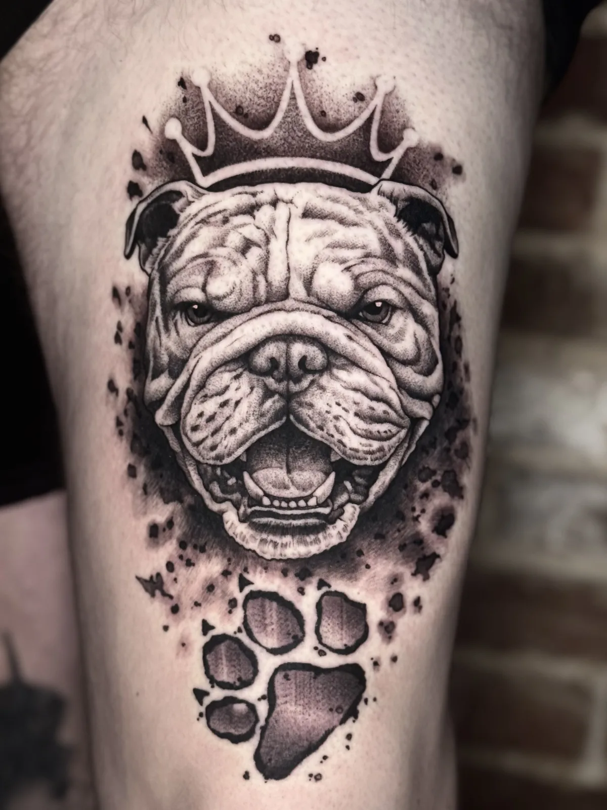 Black and grey thigh tattoo of a bulldog wearing a crown, with paw prints