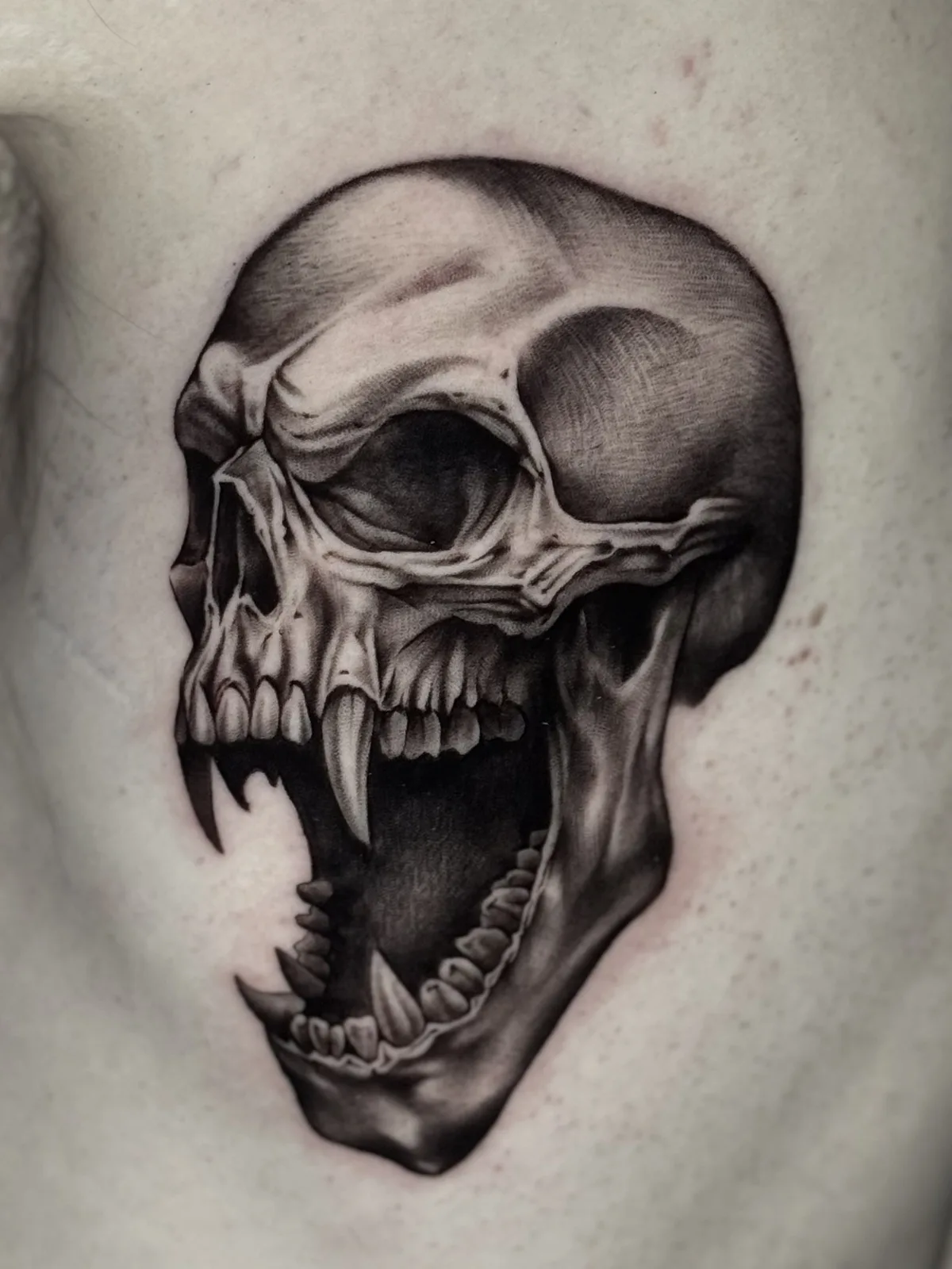Black and grey realism tattoo of a screaming skull with fangs