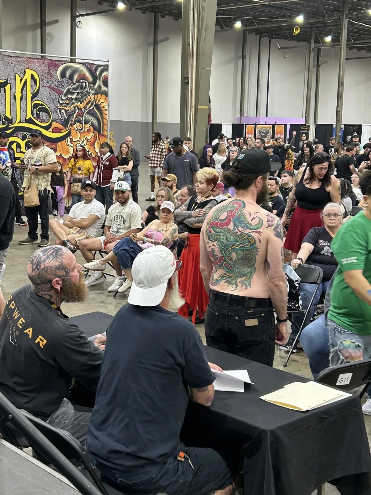 Eike Schumacher at the judges table looking at a contestant with a color back piece