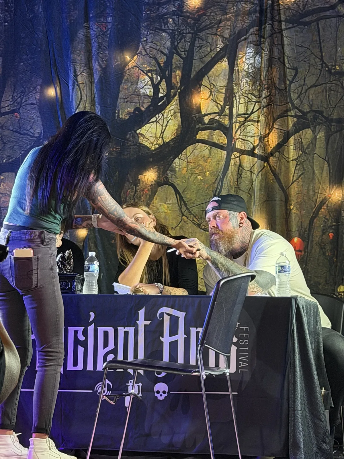 Eike Schumacher on a festival stage examining a contestant's arm tattoo