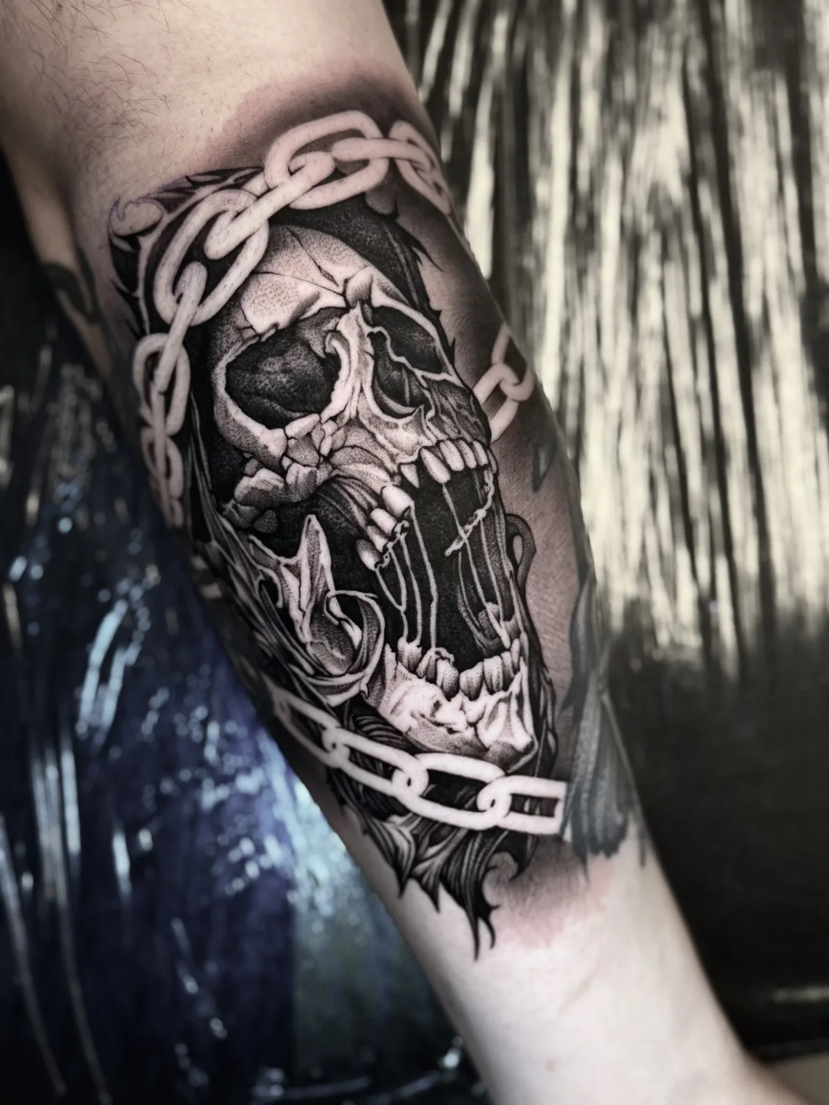 Black and grey realism tattoo of a skull wrapped in chains on the arm
