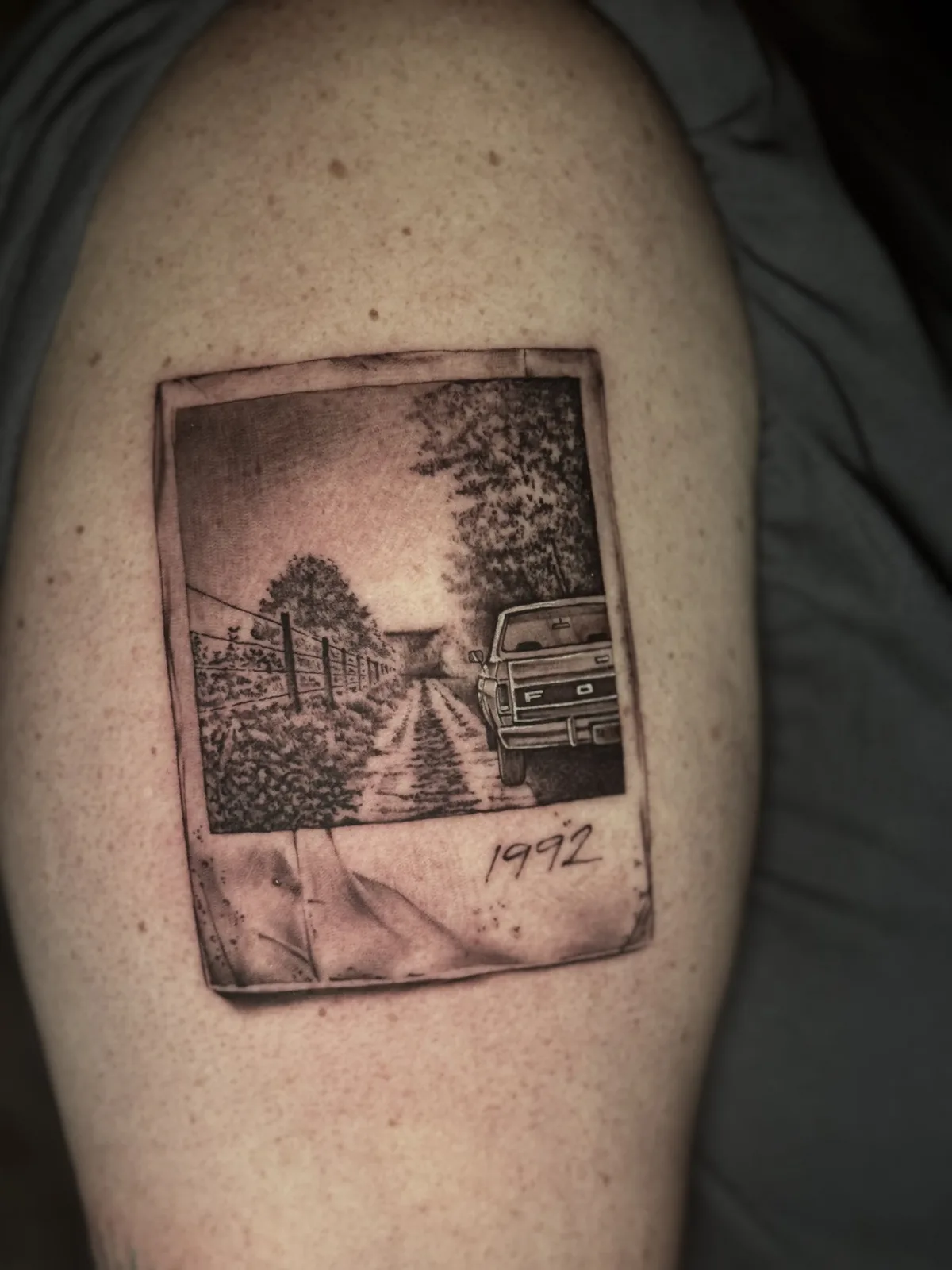 Black and grey tattoo framed as a Polaroid photo of a rural road with an old truck, dated 1992