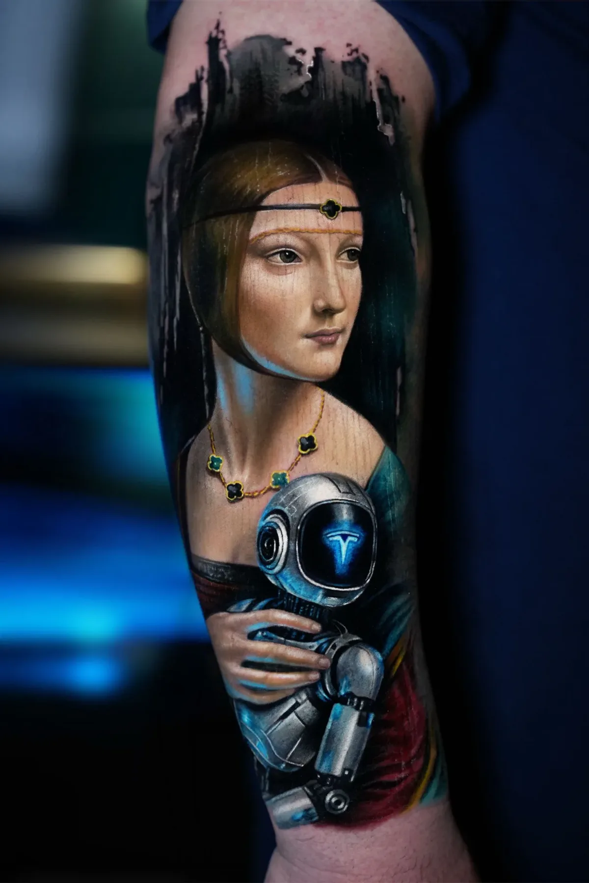 A hyperrealistic colour tattoo on an arm showing a Renaissance-style woman with a jewelled headband holding a metallic robot whose helmet displays a glowing blue T symbol; the dark abstract background suggests an industrial cityscape.